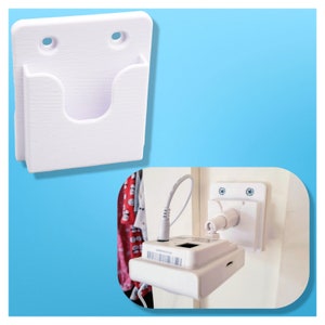 May include: White plastic wall mount with two screw holes and a rectangular cutout. A white device with a black cord is mounted on the wall.
