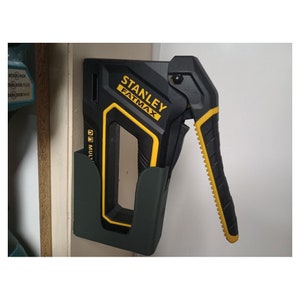 May include: A black and yellow Stanley FatMax staple gun with a green plastic holster. The staple gun is mounted on a wall.