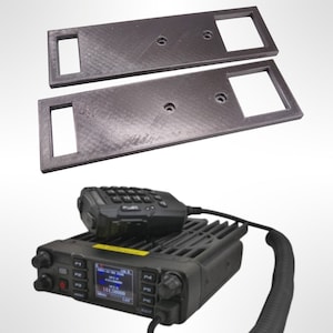 May include: Two black plastic mounting brackets with rectangular cutouts and screw holes. A black handheld radio transceiver with a keypad and a display screen.