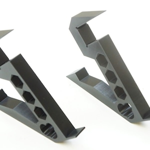 May include: Two black plastic phone stands with a honeycomb design. The stands are angled to create a raised platform for a phone.