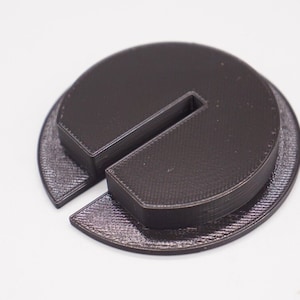 May include: A dark brown plastic circle with a split in the middle, creating a C-shape. The circle is slightly raised on the edge.