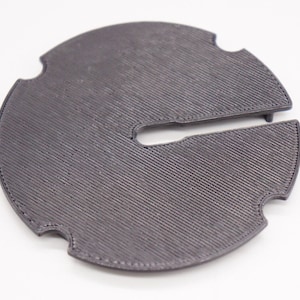 May include: A gray plastic 3D printed disc with a cutout in the center. The disc has a textured surface and three small tabs around the edge.