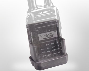 Pode incluir: Um transceptor Yaesu de banda dupla preto com uma base de carregamento preta e cinza. O transceptor tem um visor digital que mostra a frequência "CB3 446.500".