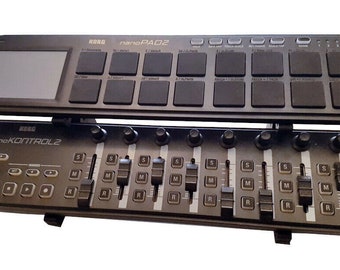 以下が含まれることがあります： 黒いKorg nanoKONTROL2と黒いKorg nanoPAD2の音楽コントローラーが積み重ねられています。nanoKONTROL2には8つのフェーダー、8つのノブ、いくつかのボタンがあります。nanoPAD2には小さな画面と16個のパッドがあります。