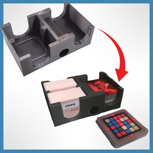 May include: A gray plastic organizer for a board game with two compartments for cards and a separate compartment for tokens. The organizer is shown assembled and disassembled. The text "BAND" is visible on the organizer.