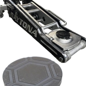 May include: A silver and black car jack with the word "DAYTONA" printed on the side. The jack is designed to lift a car for tire changes or other repairs. A black rubber pad with a hexagonal pattern is included.