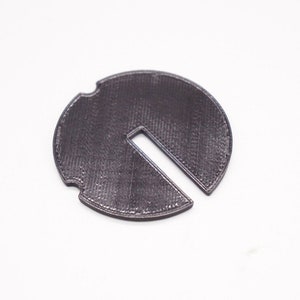 May include: A dark gray plastic disc with a cut-out section. The disc has a textured surface.