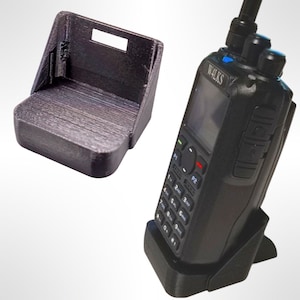 May include: A black two-piece charging stand for a two-way radio. The stand is made of 3D printed plastic. The radio has a black and grey keypad and a screen that says "WALKS".