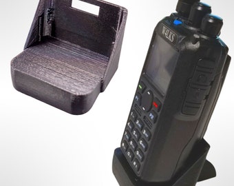 Pode incluir: Um suporte de carregamento preto de duas peças para um rádio bidirecional. O suporte é feito de plástico impresso em 3D. O rádio tem um teclado preto e cinza e uma tela que diz "WALKS".
