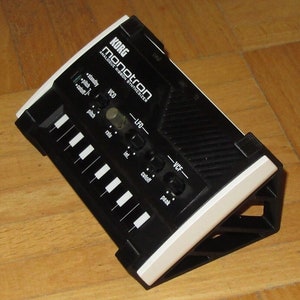 May include: A black Korg Monotron Analogue Ribbon Synthesizer with a white trim. The synthesizer has a small keyboard with 8 keys, a few knobs, and a speaker.