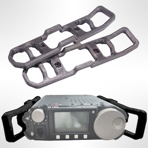 May include: Two black 3D printed brackets designed to hold a radio transceiver. The brackets are stacked on top of each other. Below the brackets is a black radio transceiver with a grey screen and a large grey knob. The radio has a microphone and a network port.