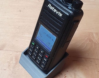 Pode incluir: Um rádio bidirecional preto com uma base de carregamento. O rádio tem um ecrã que mostra "of 26226 No CH 12 10 45:37" e um teclado com números e símbolos.