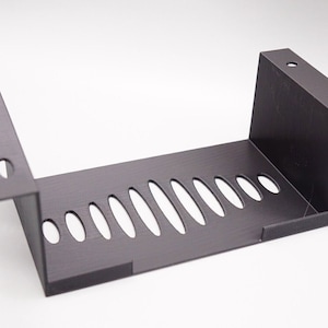 May include: A black plastic shelf with a rectangular shape and a series of oval cutouts. The shelf has two vertical sides and a flat bottom.