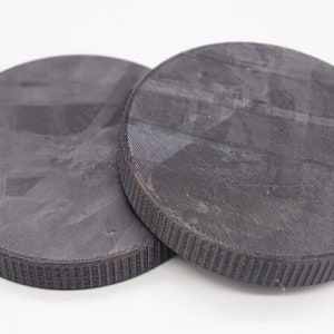 Op de afbeelding: Twee ronde, zwarte, getextureerde magnetische schijven.