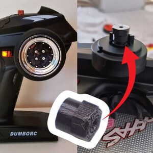 Op de afbeelding: Een zwarte afstandsbediening voor een speelgoedauto met een zilveren wiel en het woord "DUMBORC" gedrukt op de basis. Een close-up van een zwart schroefdraaddeel is ook te zien.