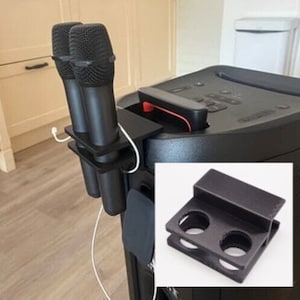 May include: Black microphone holder with two microphones attached. The holder is mounted on a black speaker.