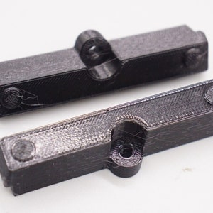 May include: Two black plastic 3D printed parts with a hole in the center and a small round knob on each end.