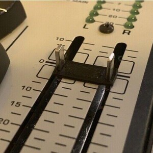 May include: Close-up of a black audio mixer with a slider control. The slider has a black plastic piece with two metal tabs. The slider has markings from 0 to 30.