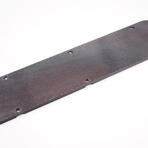 May include: A dark gray plastic cover with multiple holes and a rounded end. The cover has a textured surface.