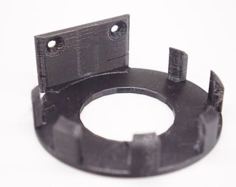 May include: A black 3D printed wall mount with a circular base and a rectangular back plate. The base has six tabs that can be used to secure the mount to a wall.