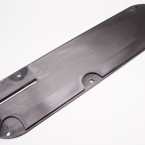 Peut inclure: Plaque en plastique noir avec plusieurs trous et une fente au centre. La plaque est conçue pour une scie à table.