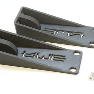 May include: Two black plastic door stops with the word "KWE" printed on them. The door stops are angled and have a small hole on the side. Four silver screws are included.
