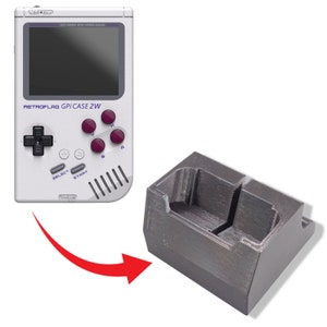 Puede incluir: Una consola de videojuegos portátil blanca y gris con una disposición de botones en blanco y negro. La consola está etiquetada como "RETROFLAG GPI CASE 2W". La consola está sobre un soporte de plástico gris.
