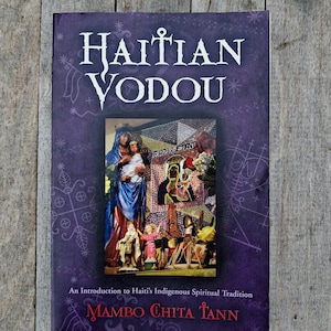 May include: A book titled "Haitian Vodou" with a purple cover. The cover features the title in white, a central image of religious figures, and the author's name, Mambo Chita Tann. The book is an introduction to Haiti's indigenous spiritual tradition.