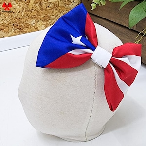 May include: A red, white, and blue bow with a white center, designed in the colors of the Puerto Rican flag.