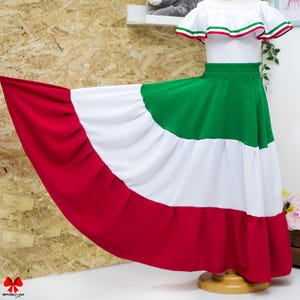 May include: A two-piece outfit featuring a white off-the-shoulder top with a ruffled neckline trimmed in green, white, and red stripes. The matching long, tiered skirt displays horizontal bands of green, white, and red fabric in a full silhouette.