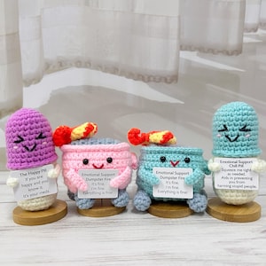 Puede incluir: Tres peluches de píldora de crochet con diferentes expresiones y mensajes. La morada dice "The Happy Pill", la rosa dice "Emotional Support Dumpster Fire" y la azul dice "Emotional Support Chill Pill".