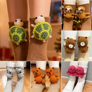 May include: A collection of crochet animal socks, including turtles, sloths, bears, koalas, tigers, and octopuses. The socks are in various colors, with the animals attached to the front of the socks. The turtles have green and yellow shells.