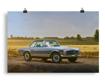 Może przedstawiać: Srebrno-szary klasyczny samochód kabriolet Mercedes-Benz zaparkowany na polu wysokiej trawy. Samochód jest zwrócony przodem do aparatu, a słońce świeci na niego.