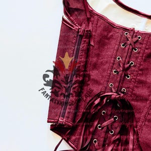 May include: Close-up of a burgundy corset with a corduroy texture. The corset features a zipper closure and ribbon lacing. The image includes the text "Fantasy Kingdom Faire ETSY".