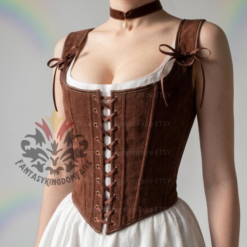 May include: A brown corduroy corset featuring a front lace-up closure with metal grommets, shoulder straps tied with ribbons, and a square neckline. The garment is worn over a white blouse and paired with a brown velvet choker featuring a pearl pendant.
