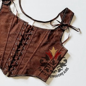 May include: A brown corduroy corset top featuring a front lace-up closure with dark brown ribbon, wide shoulder straps with ribbon ties, and a square neckline. The garment is accented with dark brown trim and a decorative logo print.