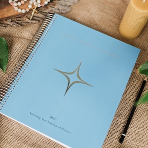 May include: A light blue spiral-bound planner with a silver star icon centred on the cover. The text "2027" and "Morning Star Liturgical Planner" is printed in small black font at the bottom. The planner features a metallic silver coil binding.