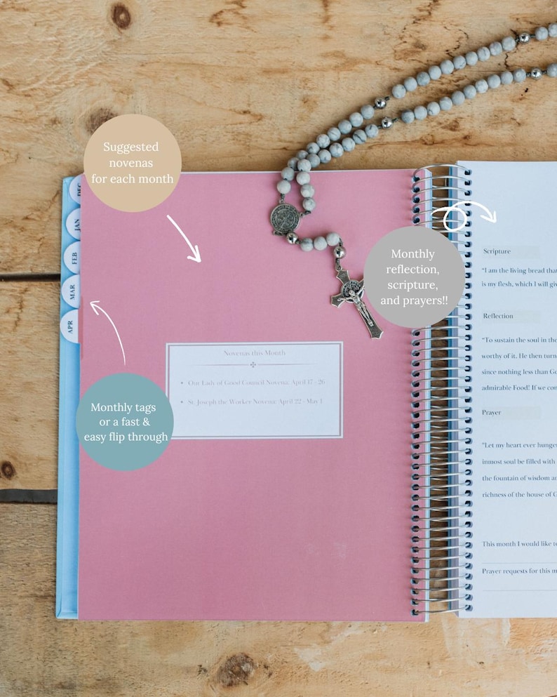 May include: Open pink spiral-bound planner with monthly tabs and a rosary. The planner includes sections for scripture, reflection, and prayers. The cover has text that says "Suggested novenas for each month" and "Monthly reflection, scripture, and prayers!!"