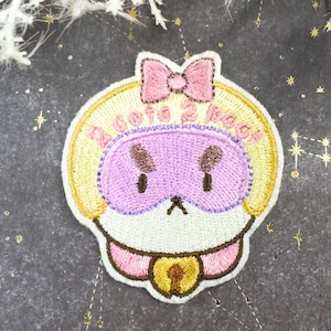 May include: Embroidered patch featuring a cartoon character with a pink sleep mask and bow. The patch has a yellow border with the text "Zzzzz 2 Pac". A pink collar with a gold bell completes the design.