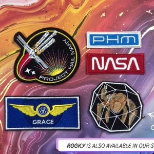 May include: A collection of embroidered patches with space and science themes. Includes a patch with the text "NASA" in white on a red background, and a patch with the text "GRACE" and wings on a blue background.