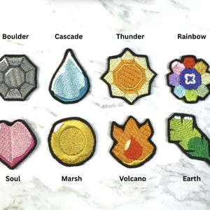 Puede incluir: Una colecci&oacute;n de parches bordados en varias formas y colores. Los parches incluyen una gema gris etiquetada como "Boulder", una l&aacute;grima azul etiquetada como "Cascade", un sol amarillo etiquetado como "Thunder" y una flor etiquetada como "Rainbow". Otros parches incluyen un coraz&oacute;n rosa etiquetado como "Soul", una moneda de oro etiquetada como "Marsh", una llama etiquetada como "Volcano" y una hoja verde etiquetada como "Earth".