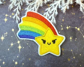 Könnte beinhalten: Ein gestickter Aufnäher mit einem gelben Stern mit mürrischem Gesichtsausdruck und einem Schweif aus regenbogenfarbenen Streifen in Rot, Orange, Gelb, Grün, Blau und Violett, alles mit einem weißen Rand auf dunklem Hintergrund.