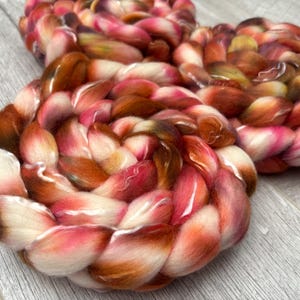 May include: Close-up of two circular fiber art pieces. The pieces are made of thick, braided yarn in shades of white, pink, orange, and brown. The yarn is soft and fluffy, with a slight sheen. The pieces are arranged on a light gray wooden surface.