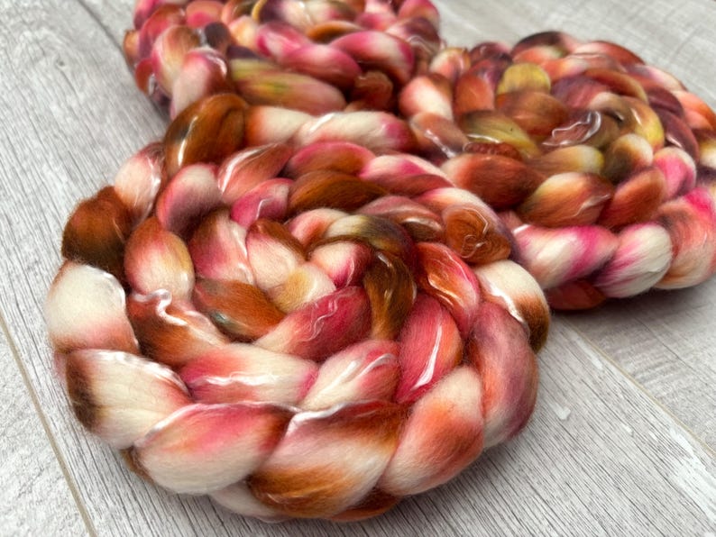 May include: Close-up of two circular fiber art pieces. The pieces are made of thick, braided yarn in shades of white, pink, orange, and brown. The yarn is soft and fluffy, with a slight sheen. The pieces are arranged on a light gray wooden surface.