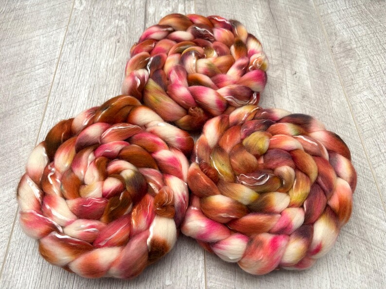 May include: Three skeins of hand-dyed yarn in a spiral arrangement. The yarn features a blend of colors, including shades of brown, pink, and white. The texture of the yarn appears soft and fluffy, ideal for knitting or crocheting projects.