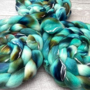 Puede incluir: Tres gruesas trenzas de lana cardada suave. El hilo presenta una paleta de colores variados de turquesa brillante, azul marino profundo y verde oliva terroso, mezclados en un patr&oacute;n de espiral continuo, suave y de textura esponjosa.