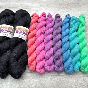 May include: A set of eight skeins of yarn in various colors, including black, coral, pink, purple, blue, and green. The yarn is arranged in a row, with the black skeins on the left and the other colors on the right. The yarn is labeled "Wonderful Wool".