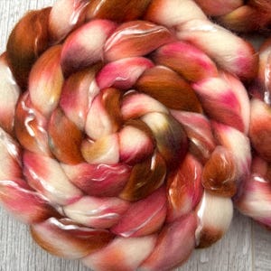 May include: Close-up of a braided skein of colorful yarn. The yarn features a blend of colors, including shades of white, pink, orange, and brown. The fibers are soft and fluffy, with a slight sheen. This yarn is suitable for various fiber art projects.