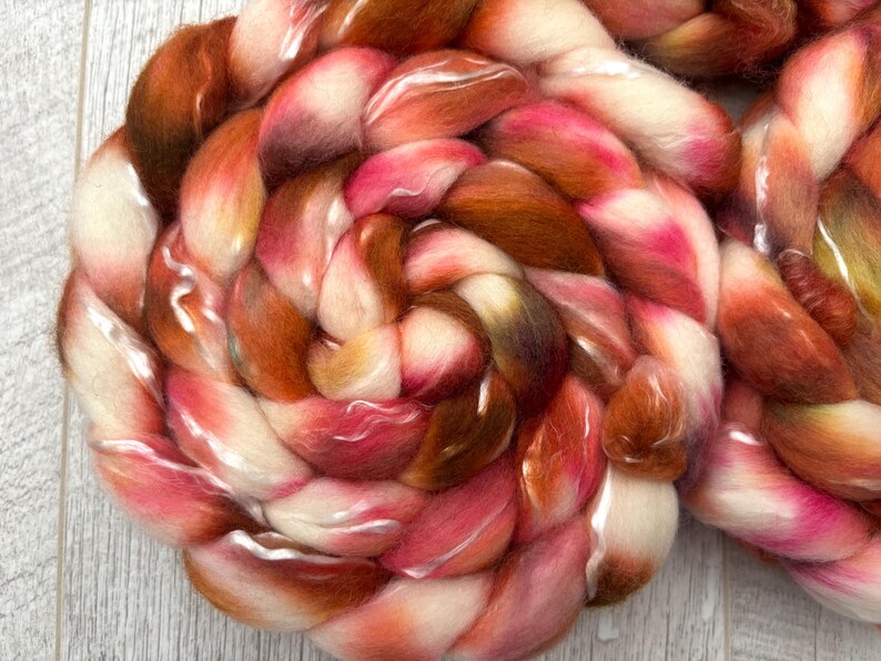 May include: Close-up of a braided skein of colorful yarn. The yarn features a blend of colors, including shades of white, pink, orange, and brown. The fibers are soft and fluffy, with a slight sheen. This yarn is suitable for various fiber art projects.