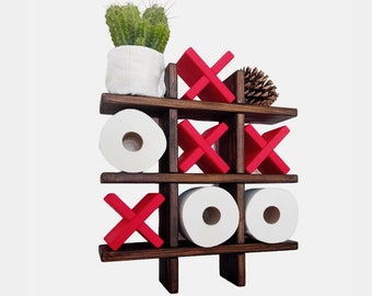 May include: A wooden wall-mounted shelf with a tic-tac-toe design. The shelf has three shelves and is painted dark brown. The shelves are decorated with red X's and O's. There are three rolls of toilet paper on the shelves. A small potted succulent plant sits on the top shelf.